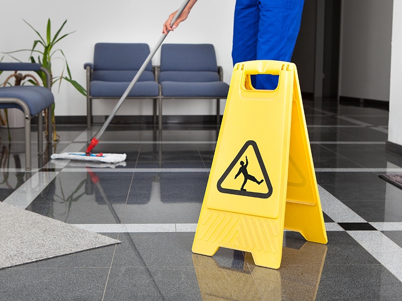 Mopping office floor with slip sign nearby