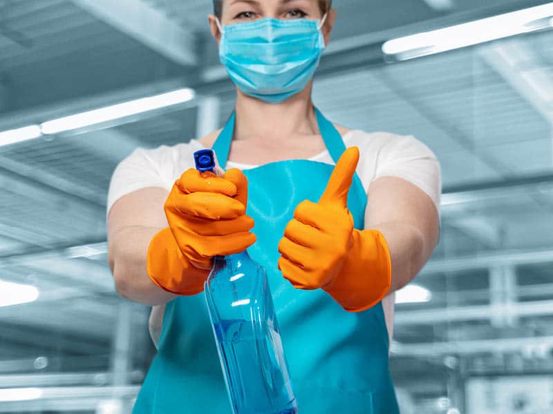 A woman in a mask and gloves with her thumbs up is ready to clean a GP surgery or medical centre.